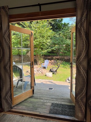 Een houten terras met een glazen deur naar een tuin, met een witte stoel en een houten bank.