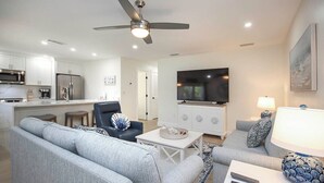 Un salon moderne avec un canapé gris, un fauteuil bleu, une table basse blanche et un téléviseur posé sur un meuble blanc.