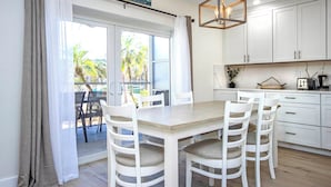 Une cuisine moderne avec des meubles blancs, une table à manger en bois et quatre chaises blanches dotées d’assises rembourrées.