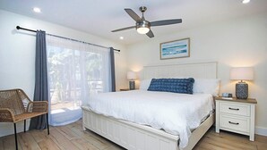 Une chambre à coucher comprenant un lit, des tables de chevet, une chaise, un ventilateur de plafond et une fenêtre avec des rideaux.