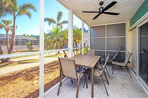 Une terrasse couverte avec une table et des chaises, de grandes fenêtres et un ventilateur de plafond.