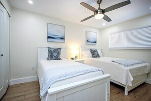 Une chambre avec deux lits, un ventilateur de plafond et des œuvres d’art accrochées aux murs.