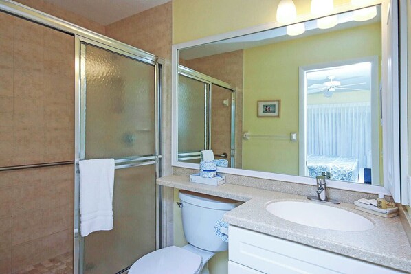 A bathroom with a glass shower enclosure, a white toilet, a sink with a mirror, and a towel hanging on the shower door.