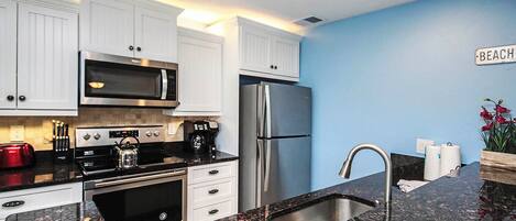 A modern kitchen with white cabinets, stainless steel appliances, and a granite countertop.