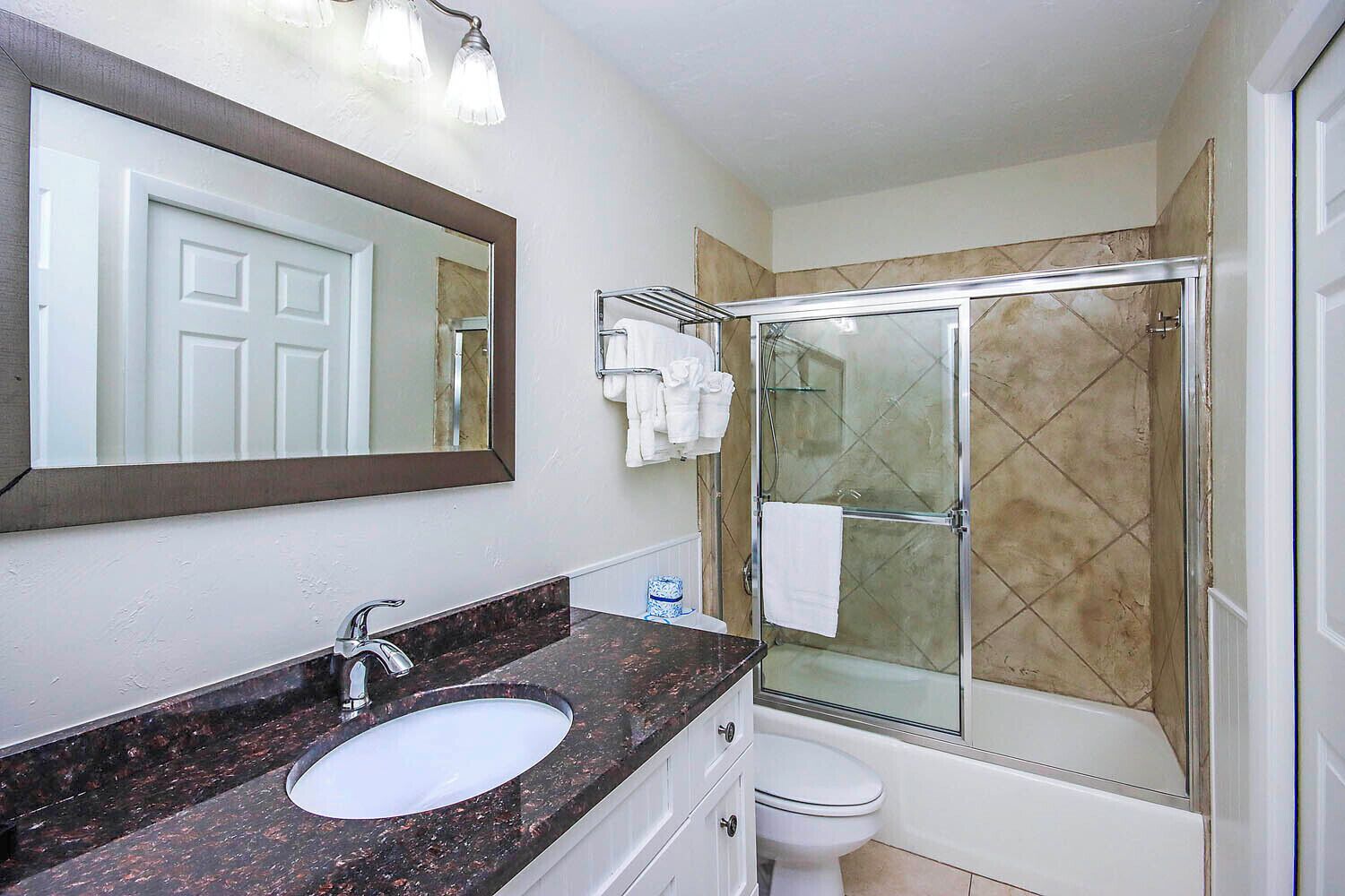 A bathroom with a marble sink, a large mirror, a glass shower enclosure, and a toilet.