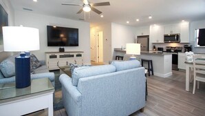 Una sala de estar moderna con un sofá, una mesa de centro y un televisor. Cuenta con una zona de cocina con armarios y un microondas.