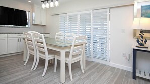 Una cocina moderna con armarios blancos, una mesa de comedor con cubierta de vidrio y un juego de sillas blancas.