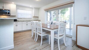 A modern kitchen with white cabinets, a wooden dining table, and white chairs. - Tranquil Sanibel Arms West Garden Unit J4 | Lush Gardens, Quick Walk to Beach (Sanibel)