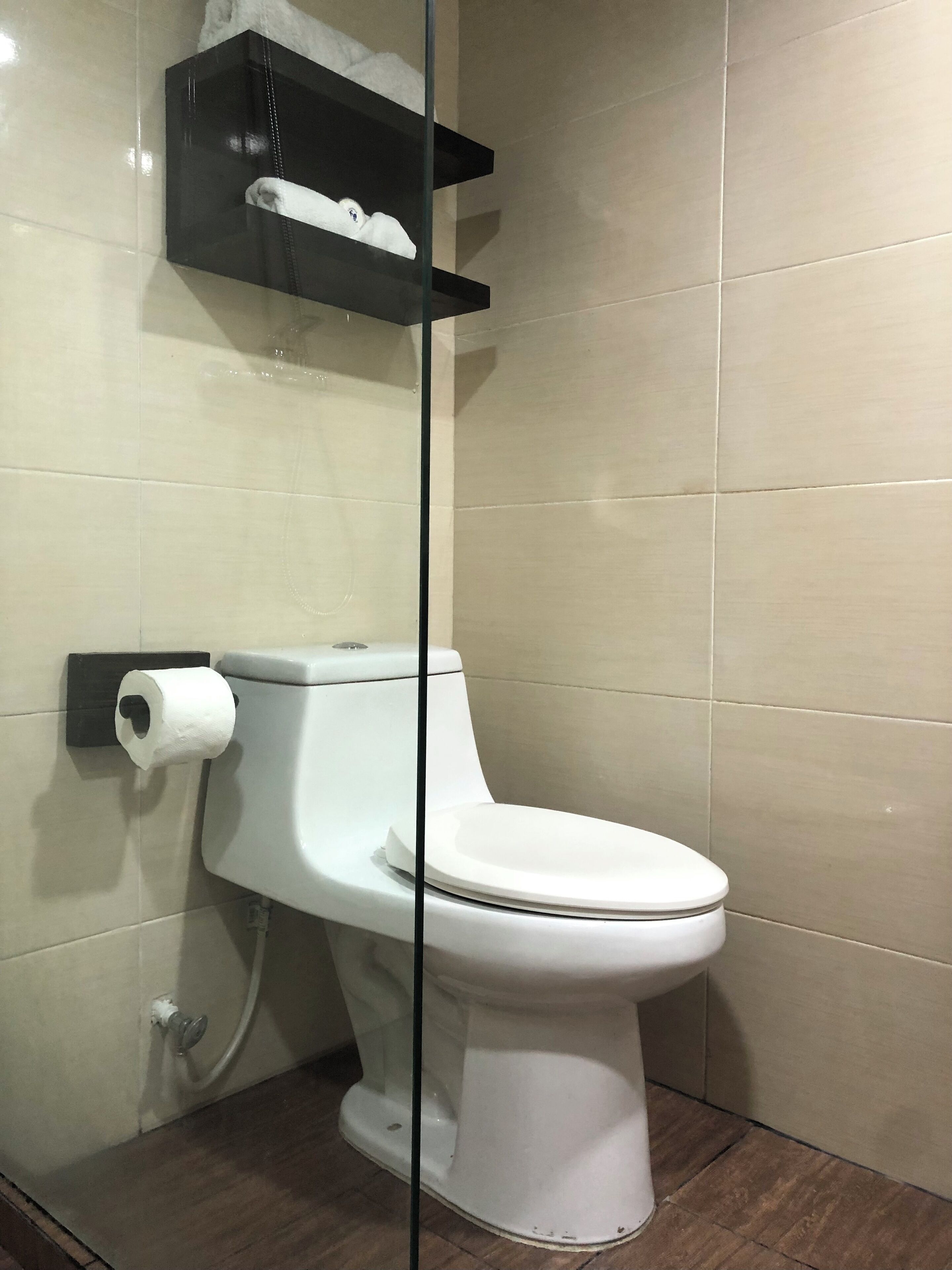 A toilet with a white seat and lid, a roll of toilet paper, and a black shelf above it.