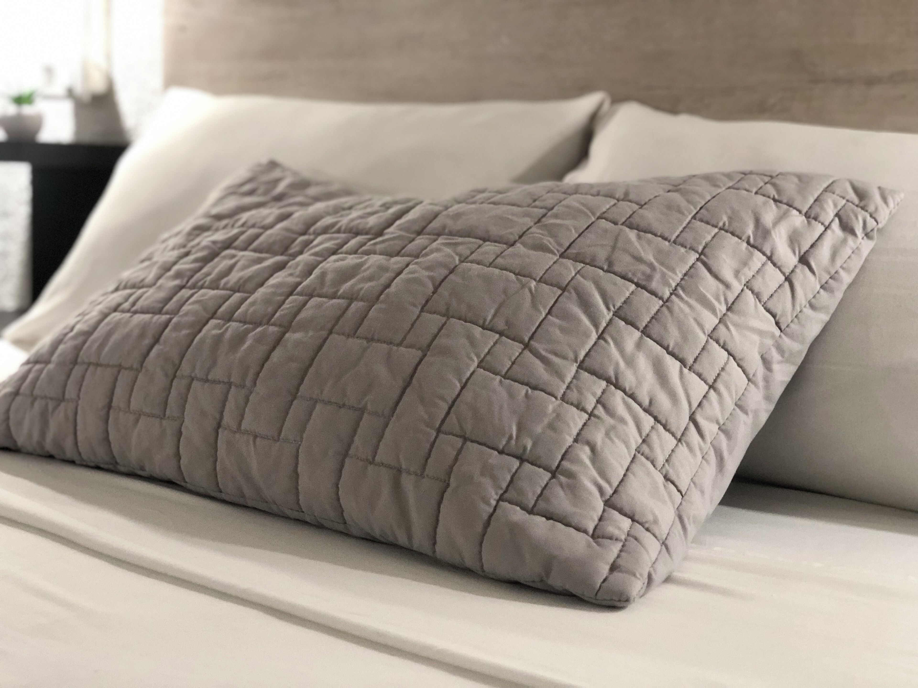 A bed with a quilted pillow and a plain white pillow.