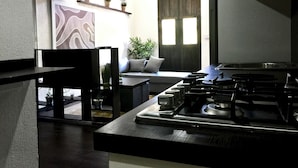 A modern kitchen with a gas stove, a dining area with a sofa and a plant, and a wall with a decorative piece. - MOKA HOUSE (Santo Domingo)