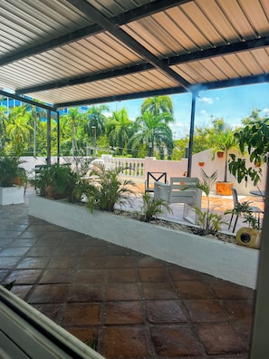 A covered patio area with a view of a garden and palm trees. - MOKA HOUSE (Santo Domingo)