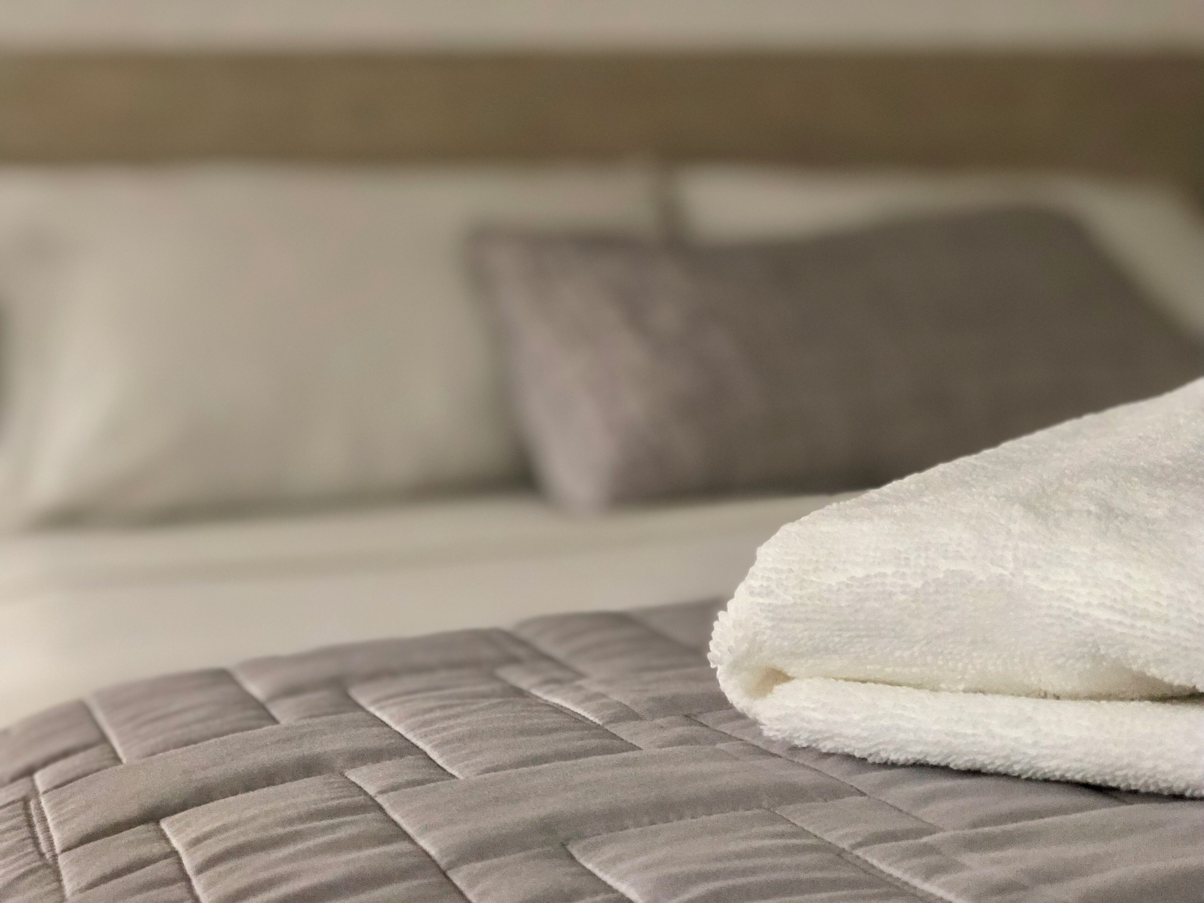 A neatly made bed with a quilted headboard and a folded white towel on the pillow.