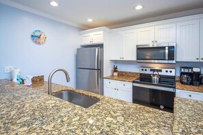A kitchen with granite countertops, stainless steel appliances, white cabinetry, and a wall clock. - Relax in Peaceful Paradise Five Minutes From the Beach (Sanibel)
