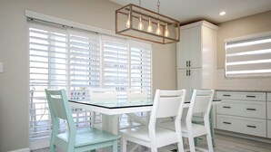 A modern kitchen with white cabinetry, a glass-top dining table, and teal chairs.