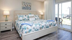 Une chambre à coucher comprenant un lit, deux tables de chevet, un ventilateur de plafond et une grande fenêtre donnant sur l’extérieur.