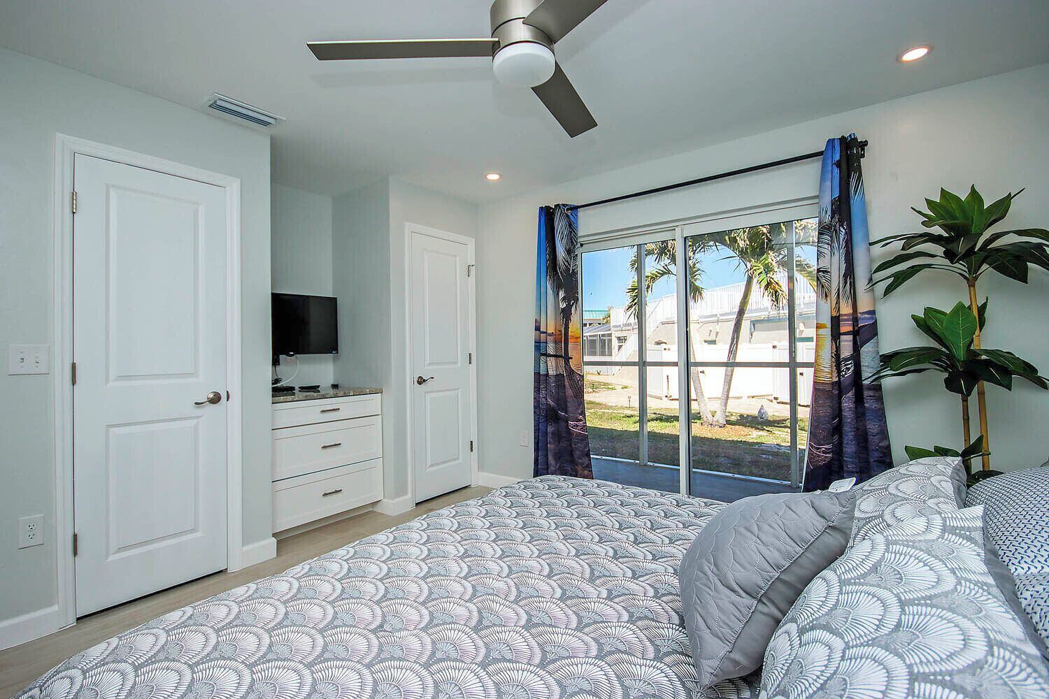 A bedroom with a bed, a TV, a ceiling fan, and a window with curtains.