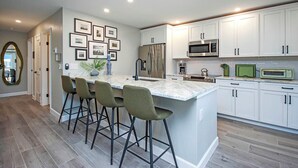 A modern kitchen with white cabinets, a central island with bar stools, a stainless steel refrigerator, and a microwave.