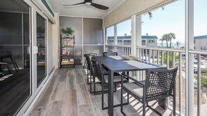 A balcony with a table and chairs, a ceiling fan, and a view of the beach.