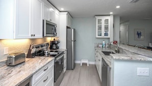 A compact kitchen with white cabinets, a stainless steel refrigerator, a microwave, and a coffee maker. - Charming Sanibel Arms West Garden Unit M1 | Short Stroll to White Sand Beach (Sanibel)