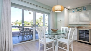 A modern kitchen with white cabinetry, a glass dining table, and a large window with a view of the outdoors. - Charming Sanibel Arms West Garden Unit M1 | Short Stroll to White Sand Beach (Sanibel)