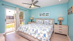 A bedroom with a bed, two bedside tables, a ceiling fan, and a sliding glass door leading to a patio. - Charming Sanibel Arms West Garden Unit M1 | Short Stroll to White Sand Beach (Sanibel)