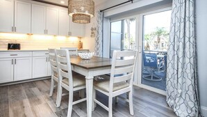 A modern kitchen with white cabinets, a wooden dining table, and a hanging light fixture. - Tropical Luxury & Poolside Perfection at Sanibel Arms West M2 (Sanibel)