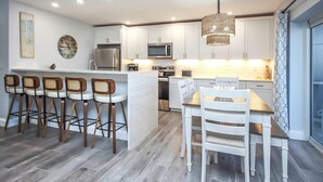A modern kitchen with white cabinetry, a central island with bar stools, and a dining table with chairs. - Tropical Luxury & Poolside Perfection at Sanibel Arms West M2 (Sanibel)