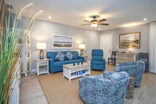 A living room with a blue sofa, matching armchairs, a coffee table, a ceiling fan, and artwork on the walls. - Relax in Peaceful Paradise Five Minutes From the Beach (Sanibel)