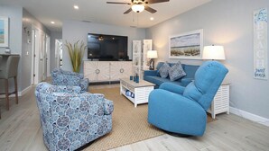 A living room with a ceiling fan, a TV, a sofa, a coffee table, and a cabinet. - Relax in Peaceful Paradise Unit M3 Steps to the Beach (Sanibel)