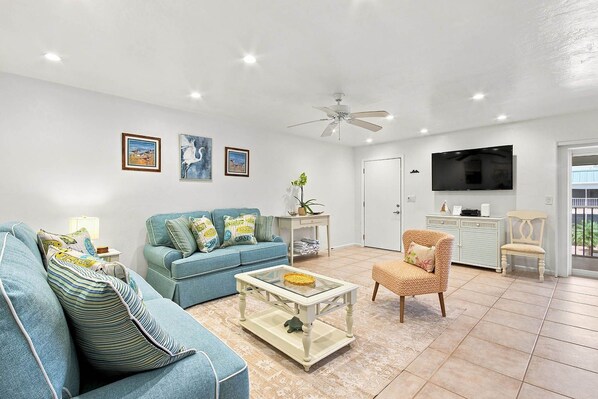 A living room with a sofa, armchair, coffee table, and a television. - Bright & Breezy Sanibel Condo With Private Beach Access (Sanibel)