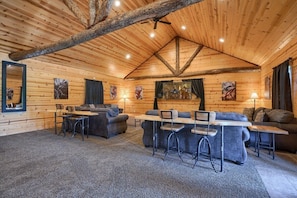 A log cabin interior with a dining area, sofas, and a ceiling with exposed beams.