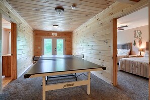 Huoneessa on pingispöytä, puuseinät, sänky ja ovi, jossa lukee ”ULOSKÄYNTI”.