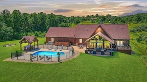 Une grande maison avec une piscine, un patio couvert et un jardin clôturé.