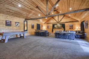 A spacious room with wooden walls and ceiling, featuring a large table, two sofas, and a bar area.