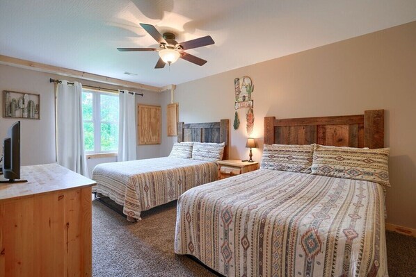 A bedroom with two beds, a ceiling fan, a TV, and a window with curtains.