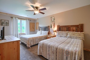 A bedroom with two beds, a ceiling fan, a TV, and a window with curtains.
