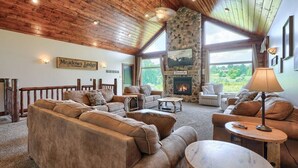 Un intérieur chaleureux, typique d’un chalet, avec une cheminée en pierre, des canapés en cuir et un plafond en bois.