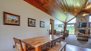 Une pièce spacieuse avec une longue table en bois et des bancs, une cheminée en pierre et des tableaux encadrés accrochés aux murs.