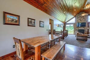 A spacious room with a long wooden table and benches, a stone fireplace, and framed pictures on the walls.