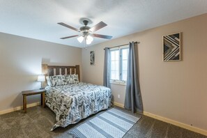 A bedroom with a bed, a nightstand, a ceiling fan, a window with curtains, and a wall art piece.