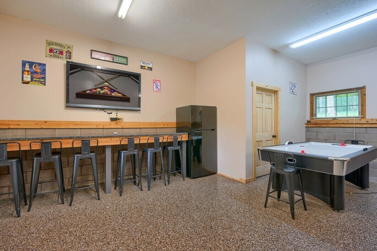 A bar area with stools, a pool table, and a refrigerator.
