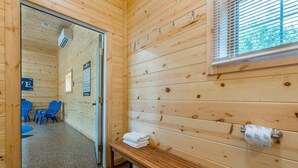 A wooden cabin with a sauna room, a bench with towels, and a window with blinds. - Wolf Den | 6BR, Indoor Pool, Arcade, Pond, Pets (Logan)