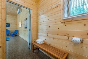 A wooden cabin with a sauna room, a bench with towels, and a window with blinds.