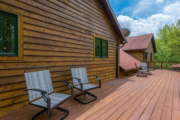 A wooden cabin with a deck, two chairs, and a satellite dish.