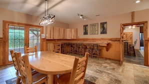 A spacious kitchen with a large wooden dining table and chairs, wooden cabinets, and a built-in island with seating. - Wolf Den | 6BR, Indoor Pool, Arcade, Pond, Pets (Logan)