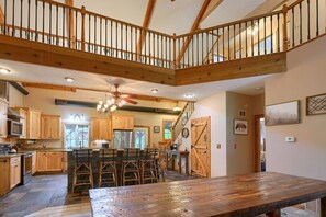 A spacious kitchen with wooden cabinets, a central island with bar stools, a dining table, and a staircase leading to an upper level.