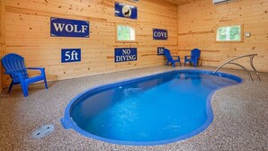 A wooden cabin with a pool, blue chairs, and signs indicating 'WOLF', '5ft', 'COVE', and 'NO DIVING'. - Wolf Den | 6BR, Indoor Pool, Arcade, Pond, Pets (Logan)