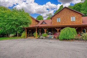 A two-story wooden lodge with a covered porch and a stone fireplace.