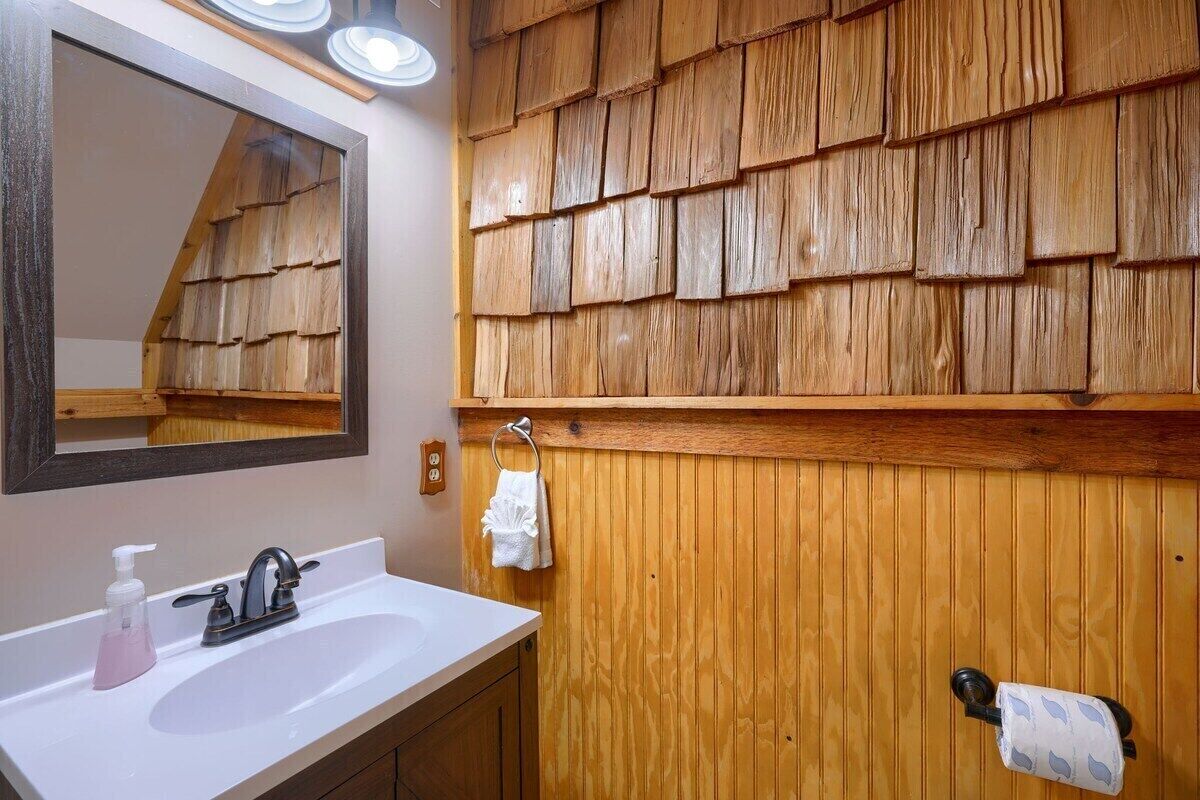 Een badkamer met een houten wandpaneel, een witte wastafel met een kraan, een spiegel en een handdoekhouder.